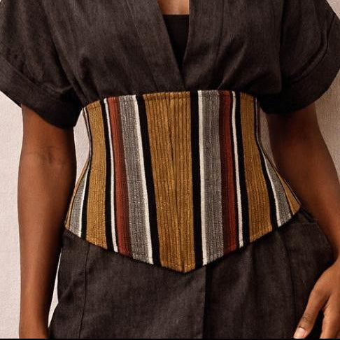 Woman wearing a dark brown outfit with a striped corset against a beige background