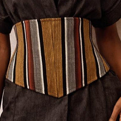 Woman wearing a dark brown outfit with a striped corset against a beige background